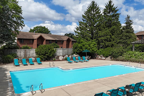 A swimming pool surrounded by lawn chairs and trees.