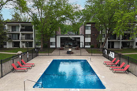 A swimming pool surrounded by red lounge chairs and trees.