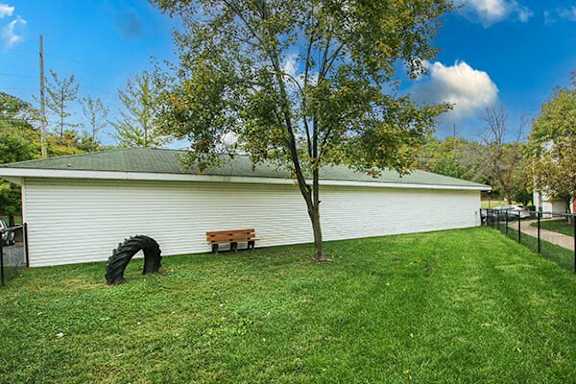 a white building with a bench and a tire in the grass