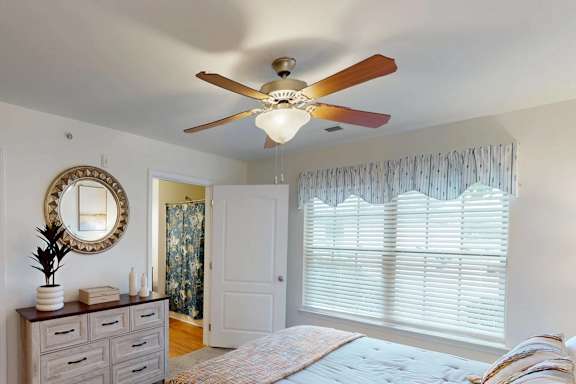 A bedroom with a bed, dresser, mirror, and window with blinds.