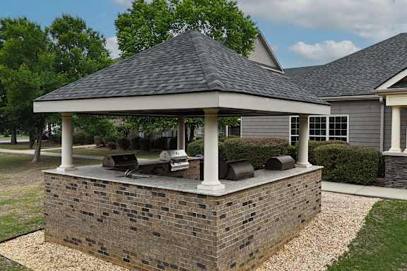 A gazebo with a stone base and a black roof is surrounded by a gravel path.