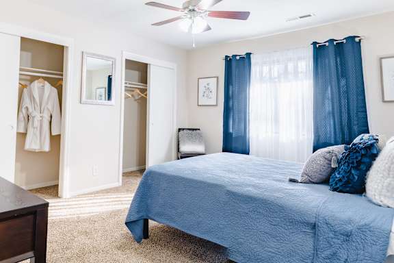 A bedroom with a blue bedspread and a white ceiling fan.