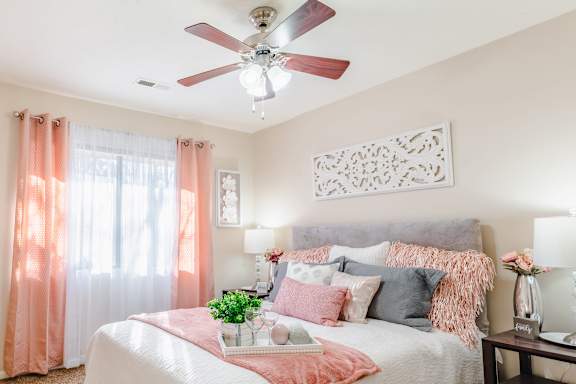 A bedroom with a bed, pillows, a ceiling fan, and a window with curtains.