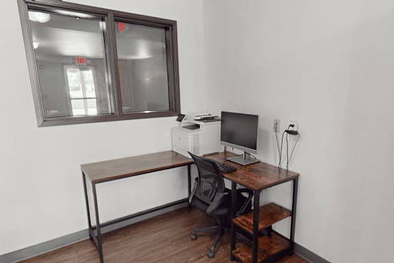 A black chair sits in front of a desk with a computer monitor and keyboard.