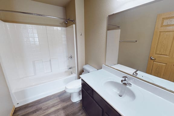 A white sink with a wooden cabinet and a white toilet in a bathroom.