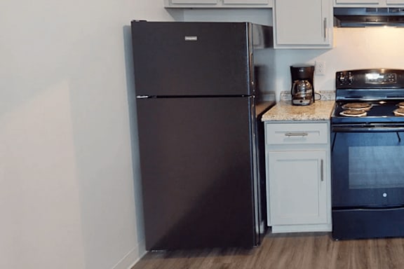 A black refrigerator is in a kitchen with a white oven and stove.