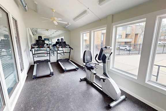 A spacious gym with treadmills, elliptical machines, and a fan.