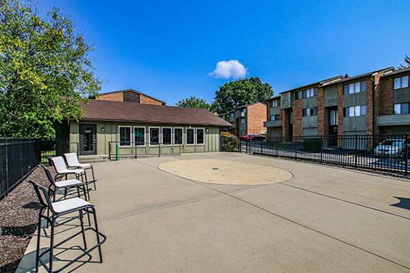 A sunny day at the outdoor basketball court with chairs and a building in the background.