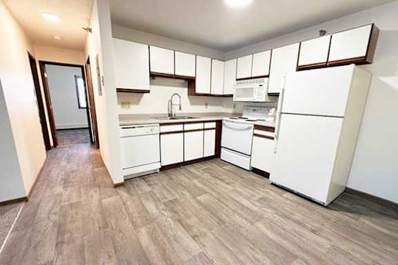 A kitchen with white appliances and wooden floors.