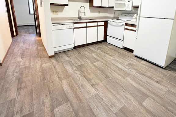 A kitchen with white appliances and wooden flooring.