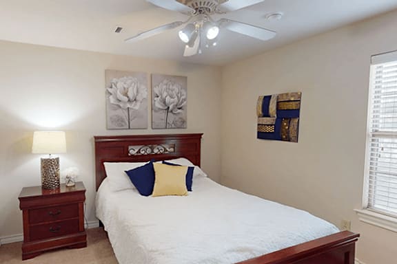 A bedroom with a bed, nightstand, and two framed pictures on the wall.