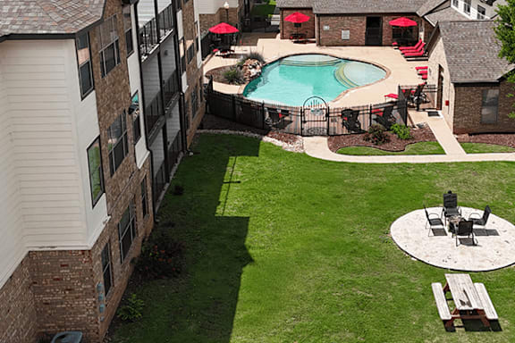 A pool with a fence and a table with chairs is surrounded by a grassy area.
