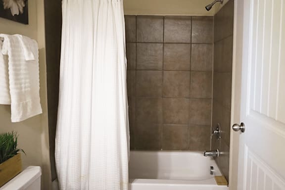 A white shower curtain hangs over a white bathtub in a bathroom.