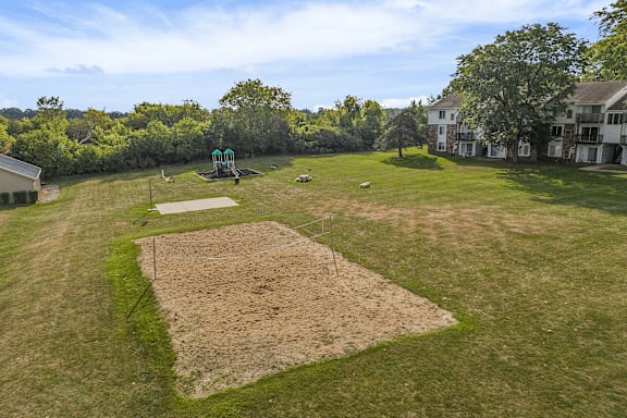 A large grassy field with a dirt mound in the center and a green structure in the background.
