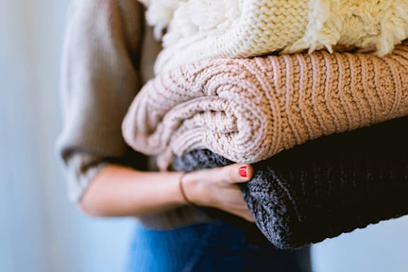 A person holding a stack of knitted sweaters.