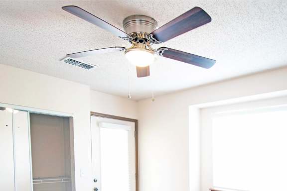 A ceiling fan with a light on in a room with white walls.