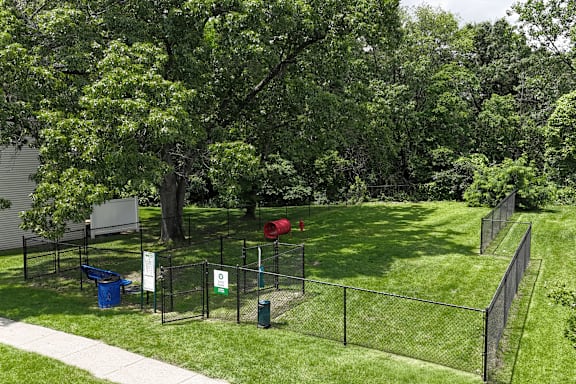 A green park with a fence and a blue trash bin.