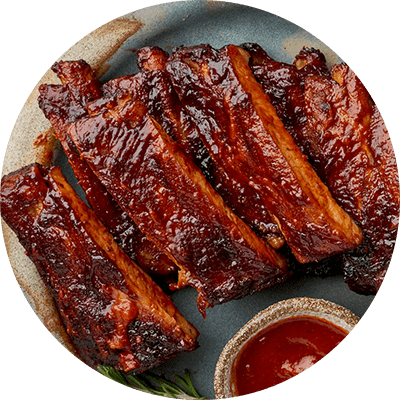 A plate of barbecued ribs with a side of sauce.