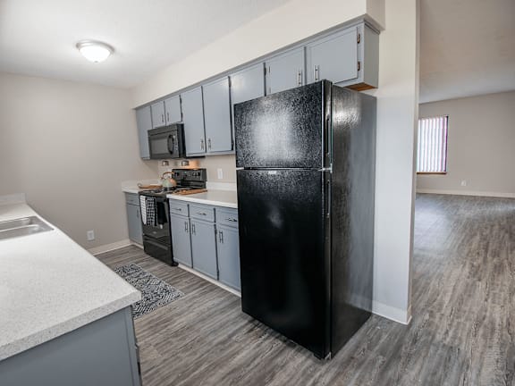 A black refrigerator stands in a kitchen with grey cabinets and a white counter.