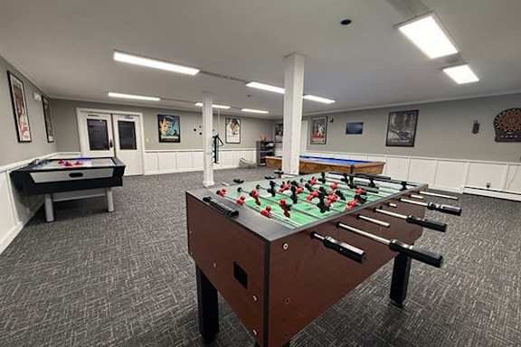 A foosball table is in the middle of a room with pool tables and a billiards table.