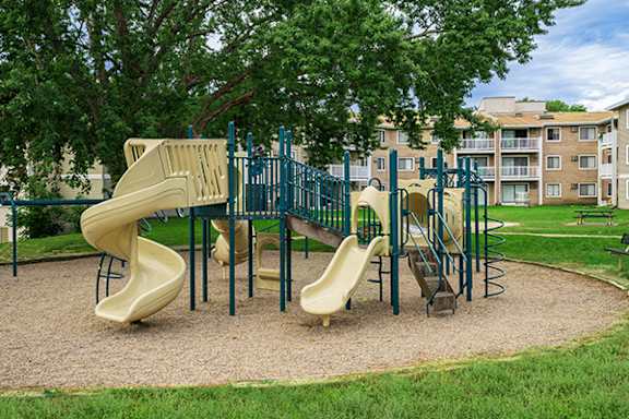 A playground with a yellow slide and green fence.