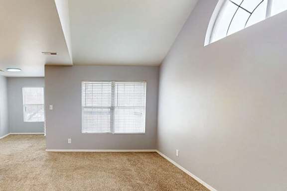 A room with a carpeted floor and a large window with blinds.