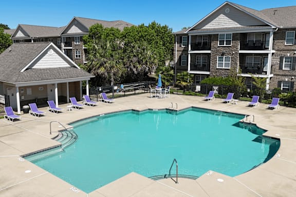 A large swimming pool surrounded by purple lounge chairs and buildings in the background.