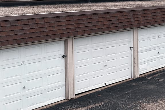 Three white garage doors are closed and lined up next to a brown roof.