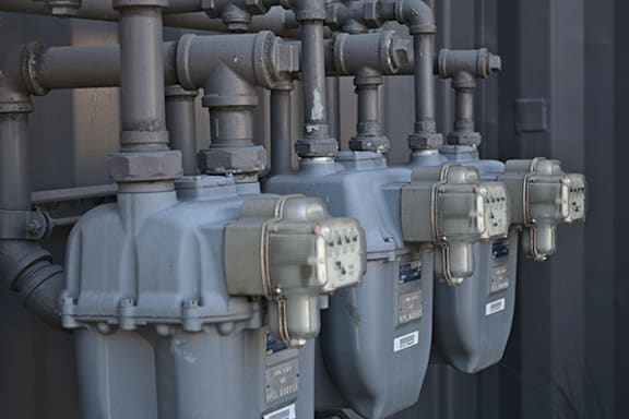 A series of grey pipes and valves are lined up on a wall.