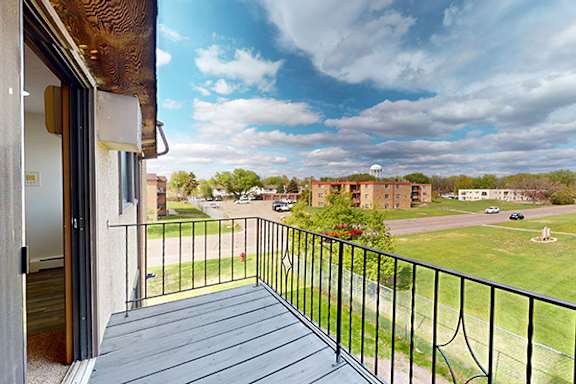 A balcony with a black railing overlooks a grassy area and buildings.