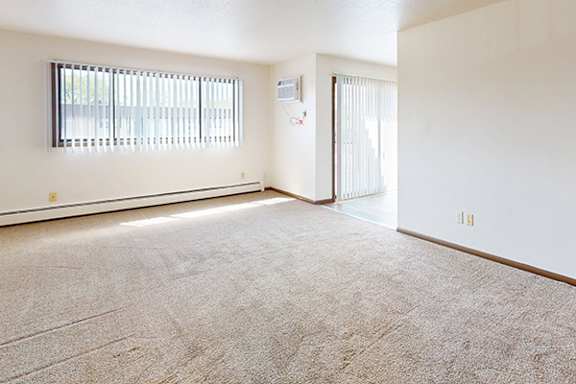 A room with a carpeted floor and a window with blinds.