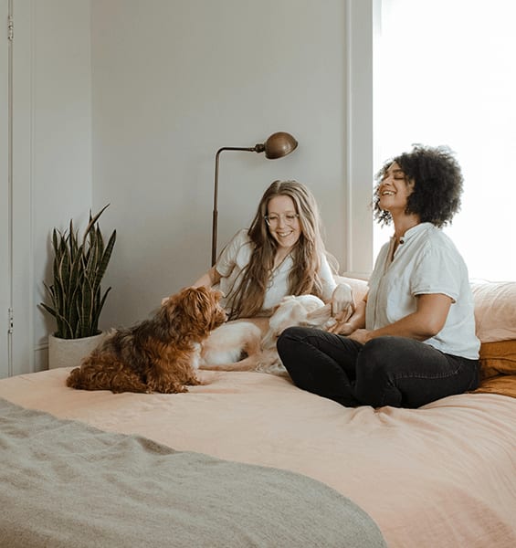 two women sitting on a bed with a dog