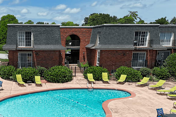 A swimming pool surrounded by yellow chairs and a brick building.