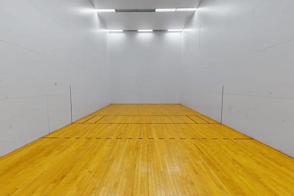 A squash court with a wooden floor and white walls.