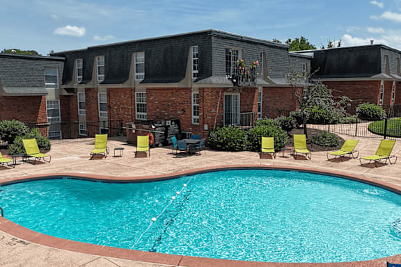 A swimming pool surrounded by yellow chairs and a brick building.