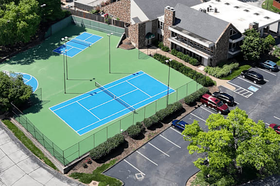A tennis court is surrounded by a parking lot and a building.
