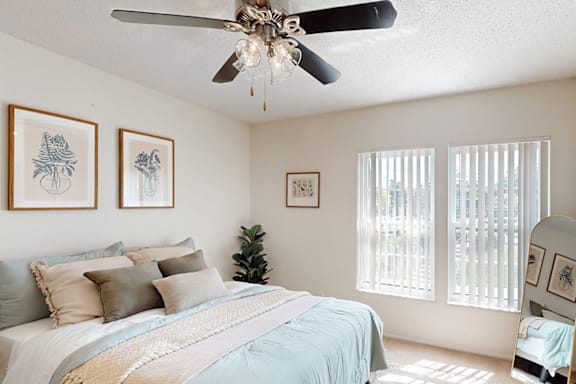 A bedroom with a bed, a ceiling fan, and pictures on the wall.