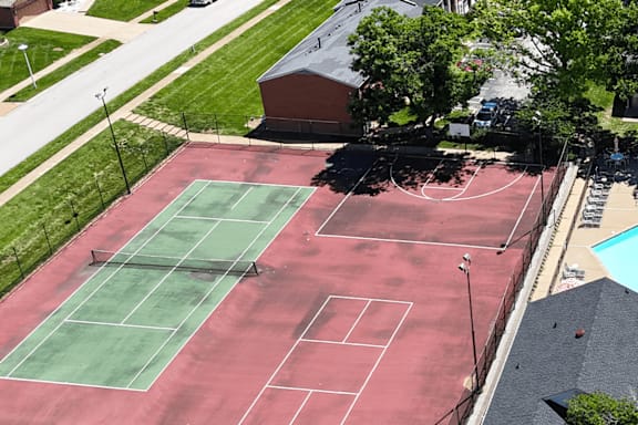 A tennis court with a red surface and green net.