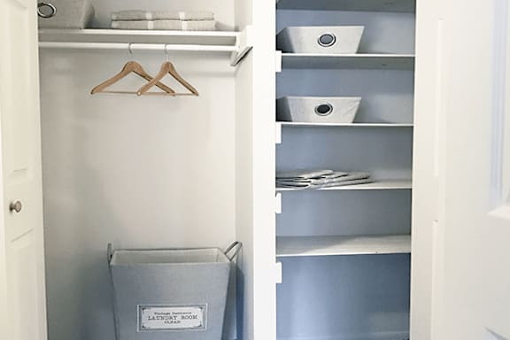 A laundry basket is in a closet with a hanger and shelves.