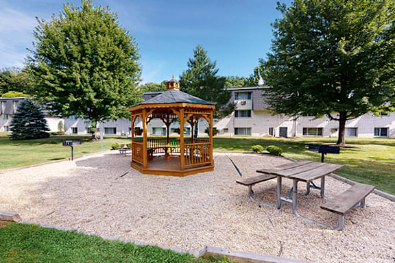 A gazebo is surrounded by picnic tables in a park.