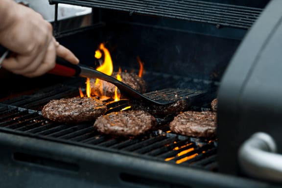 a person using a spatula to grill burgers on a grill