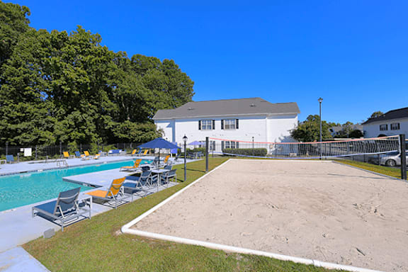 A sandy volleyball court is surrounded by a pool and a white building.