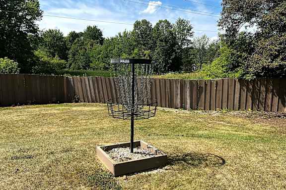 A disc golf basket sits in a box on a grassy field.