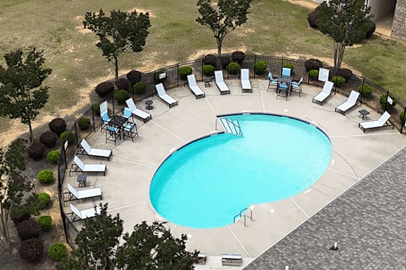 A round swimming pool surrounded by lounge chairs and trees.