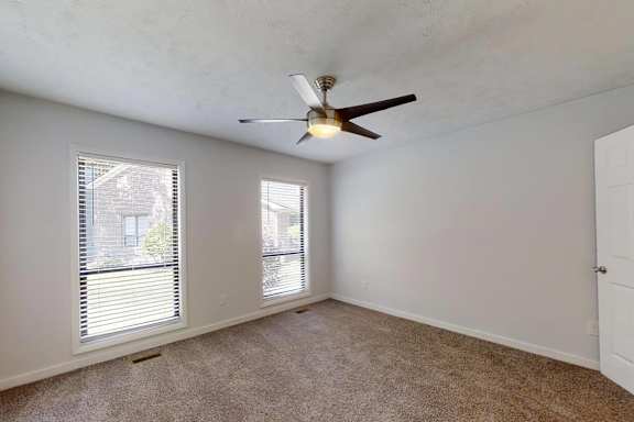 A room with a ceiling fan and two windows.
