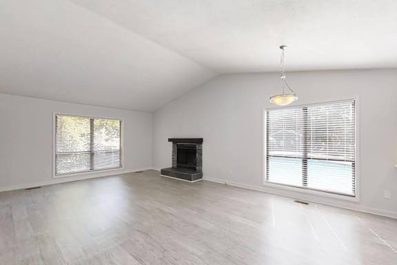 A spacious living room with a fireplace and two windows.