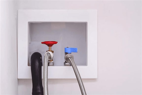 A red object is connected to a blue object with a grey hose.