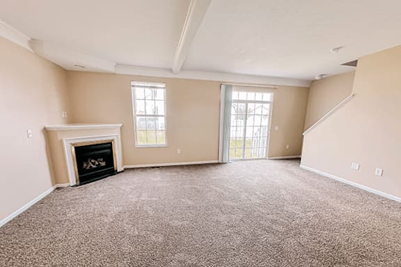 A large empty room with a fireplace and carpeted floor.