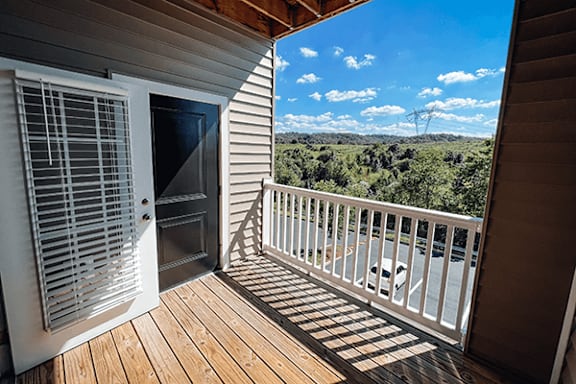 A balcony with a view of the countryside and a car parked in the driveway.