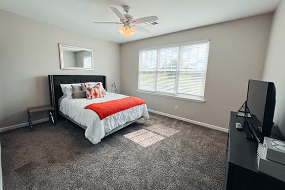 A bedroom with a bed, a television, and a window with blinds.